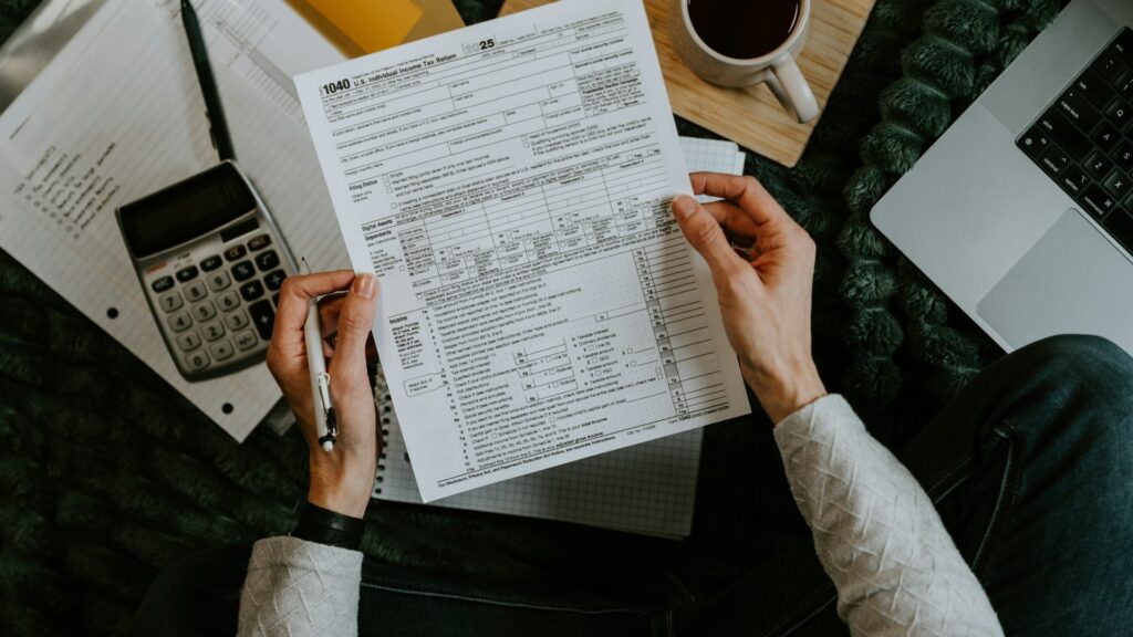 Hands holding a tax form beside a calculator and laptop.
