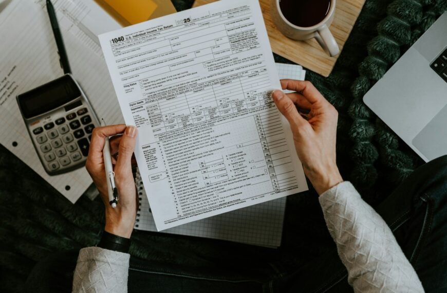 Hands holding a tax form beside a calculator and laptop.