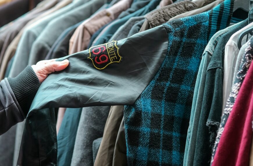 A hand holds a shirt on a crowded rack of secondhand clothes.