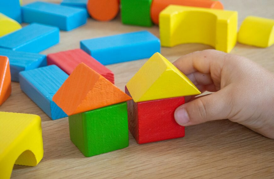 Colorful wooden toy blocks with a hand placing one.
