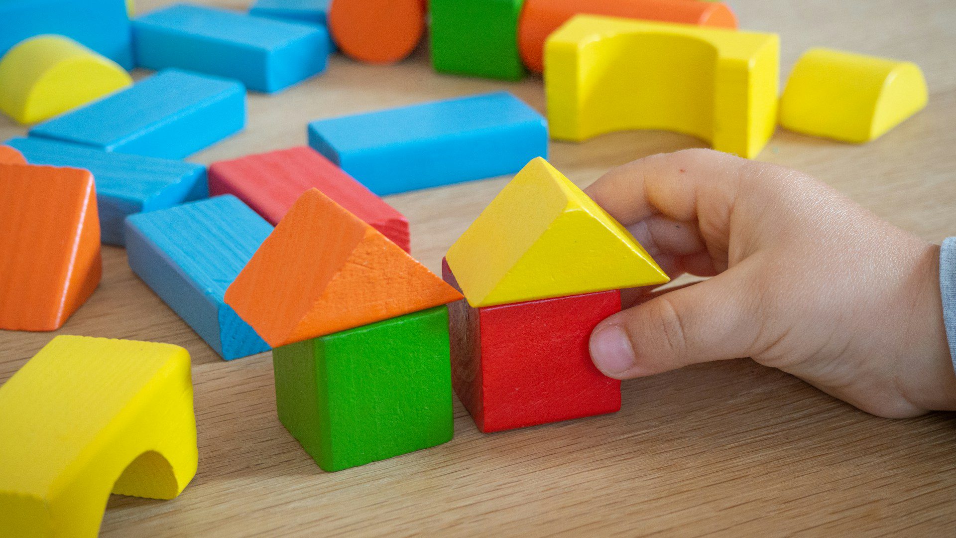 Colorful wooden toy blocks with a hand placing one.