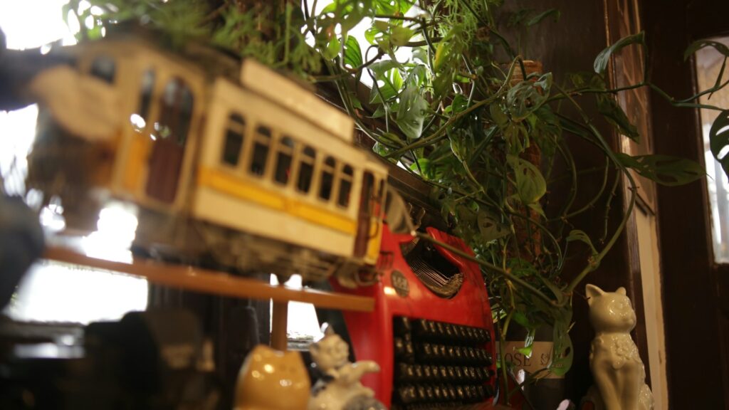 A vintage toy tram, a red typewriter and ceramic cat figurines on a shelf (Unsplash photo by MChe Lee).