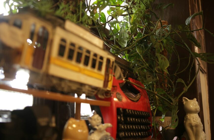 A vintage toy tram, a red typewriter and ceramic cat figurines on a shelf (Unsplash photo by MChe Lee).