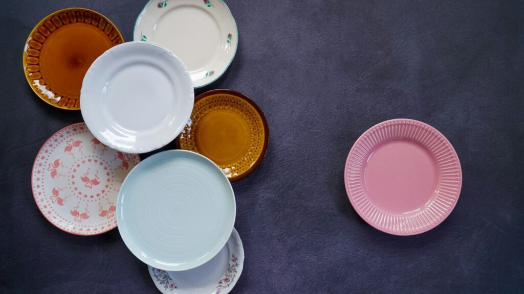 Several vintage plates in amber, pastel blue, pink and floral patterns on a dark surface (Unsplash photo by Karolina Kołodziejczak).