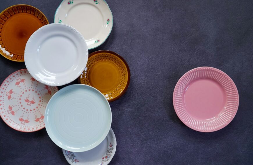 Several vintage plates in amber, pastel blue, pink and floral patterns on a dark surface (Unsplash photo by Karolina Kołodziejczak).