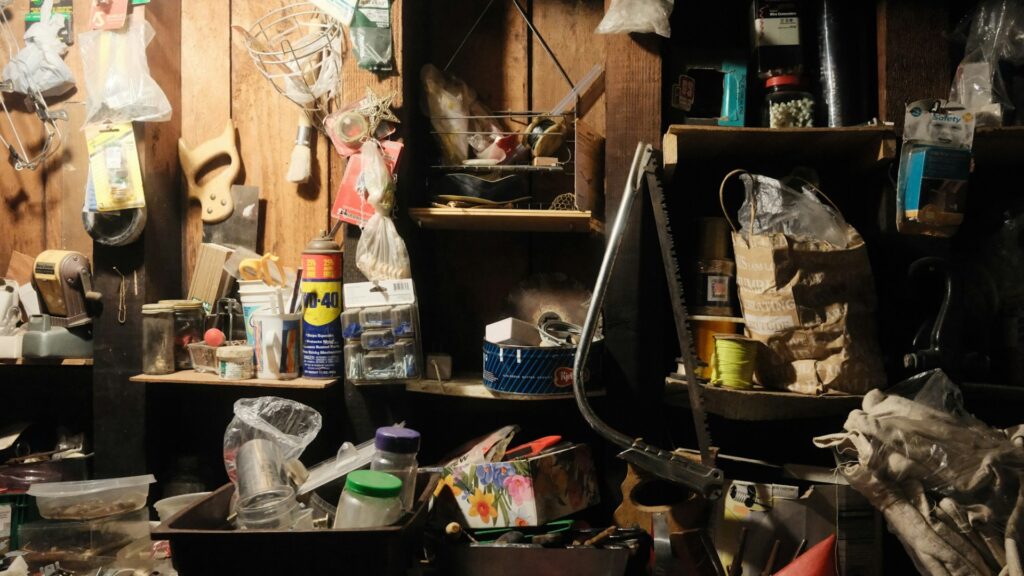 A dim, cluttered garage packed with tools, shelves and stored household items (Unsplash photo by Stephen Pontes).