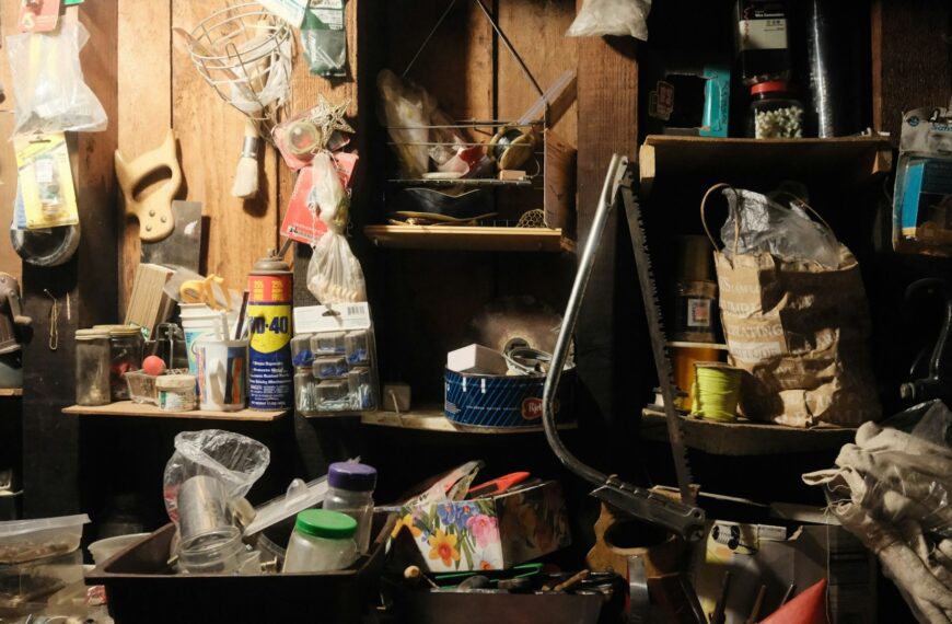 A dim, cluttered garage packed with tools, shelves and stored household items (Unsplash photo by Stephen Pontes).