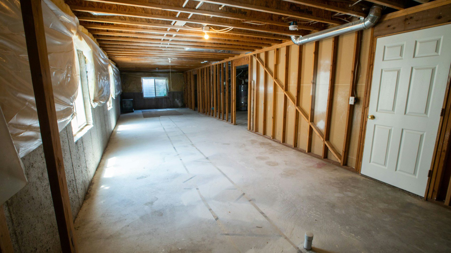An unfinished basement with exposed beams, a concrete floor and a white door (Unsplash photo by Real Twin Photos).