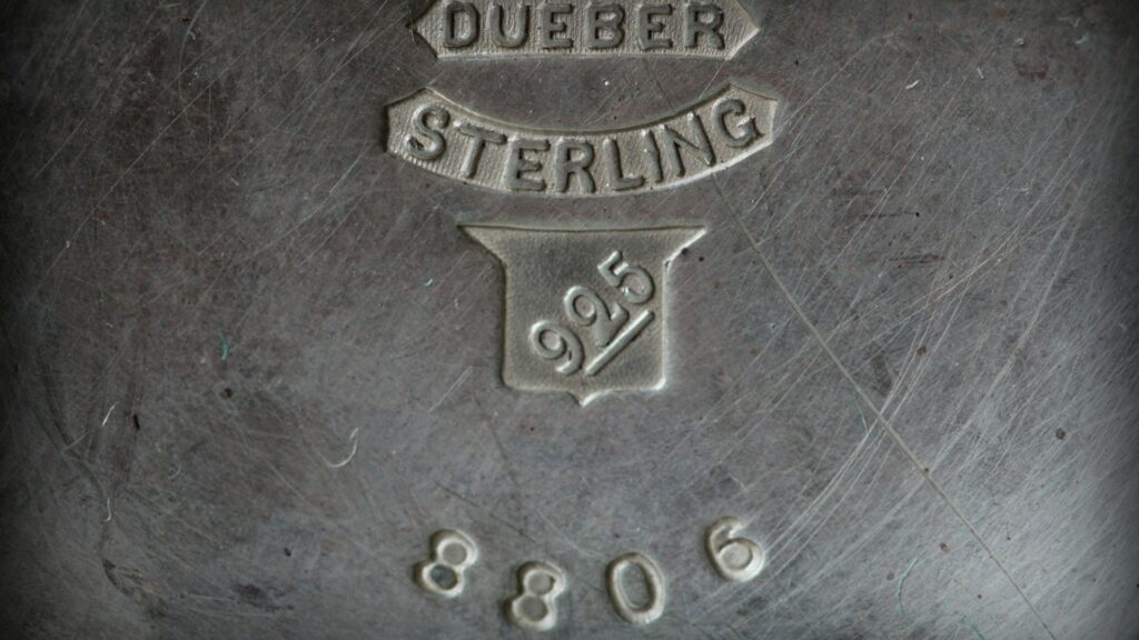 A close-up of a maker's mark stamped into sterling silver, reading Dueber Sterling 925 (Unsplash photo by Anne Nygård).