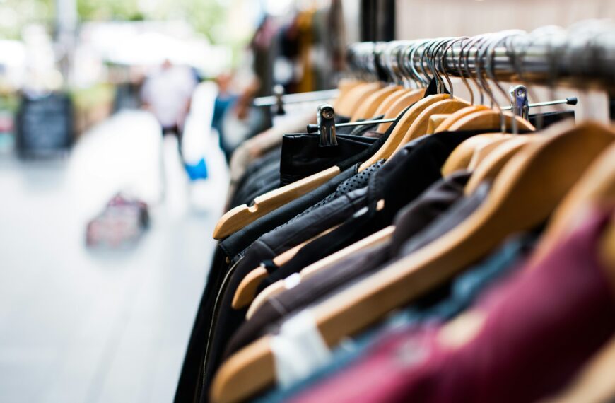 Clothes hang on hangers on a rack in a clothing store.