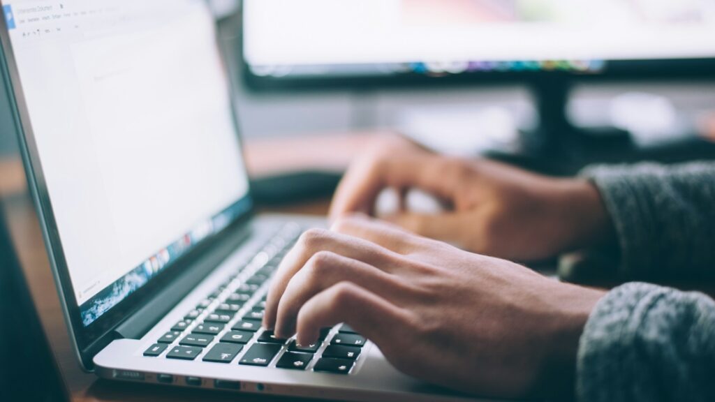 A person types on a laptop at a desk while shopping online.