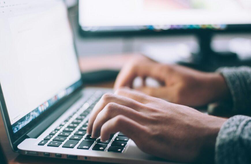 A person types on a laptop at a desk while shopping online.