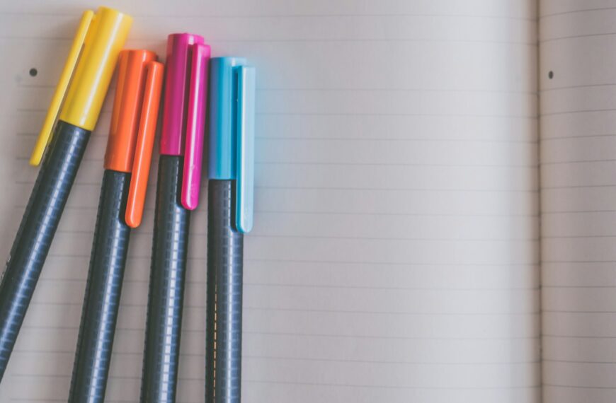 Four colorful pens lie on a sheet of lined paper.