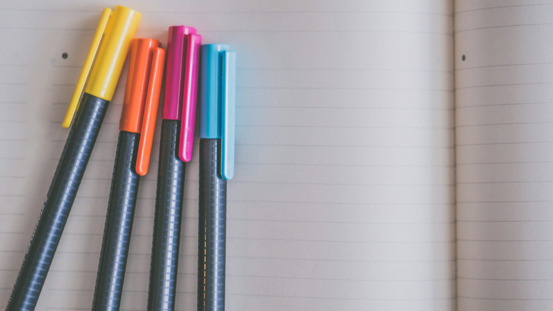 Four colorful pens lie on a sheet of lined paper.