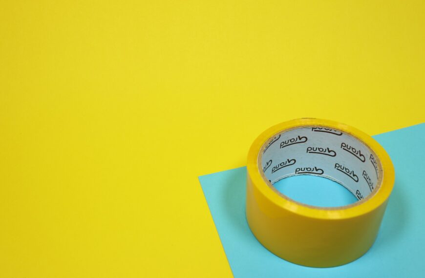 A roll of yellow packing tape rests on a blue surface.