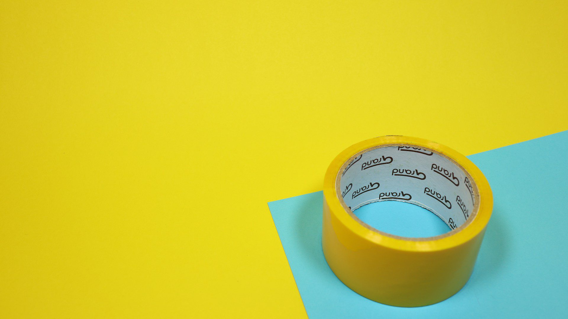 A roll of yellow packing tape rests on a blue surface.