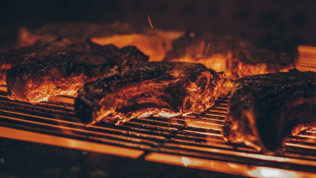 Meat cooking on a grill grate over hot coals.