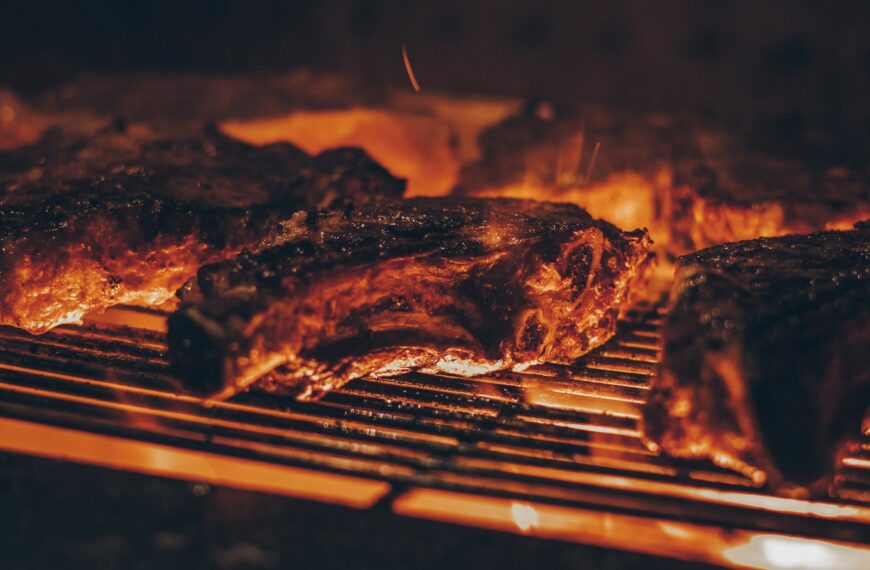Meat cooking on a grill grate over hot coals.