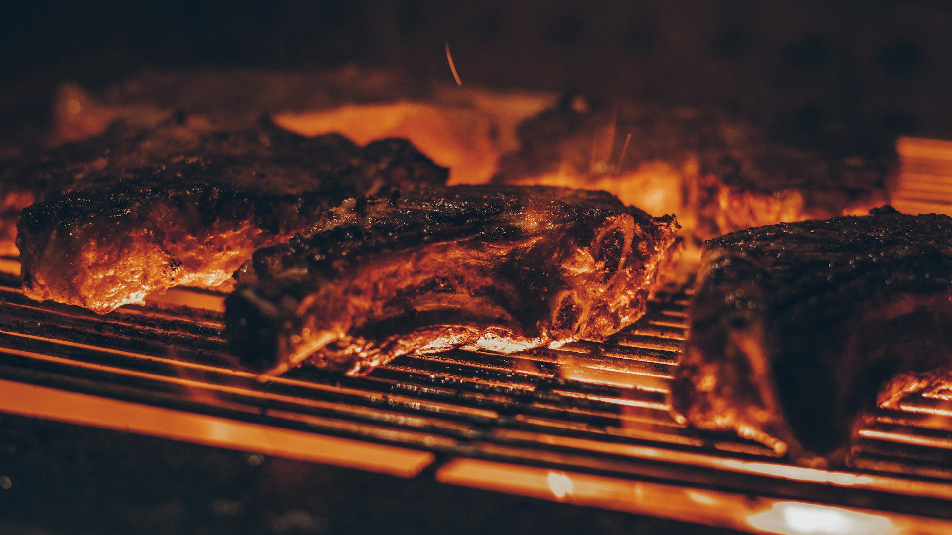 Meat cooking on a grill grate over hot coals.