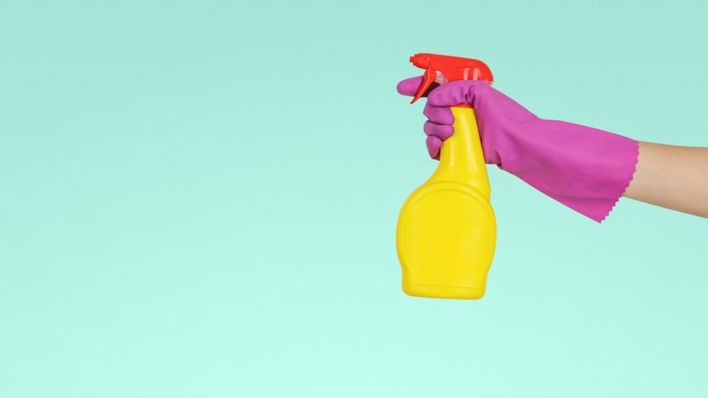 A hand holds a yellow plastic spray bottle.