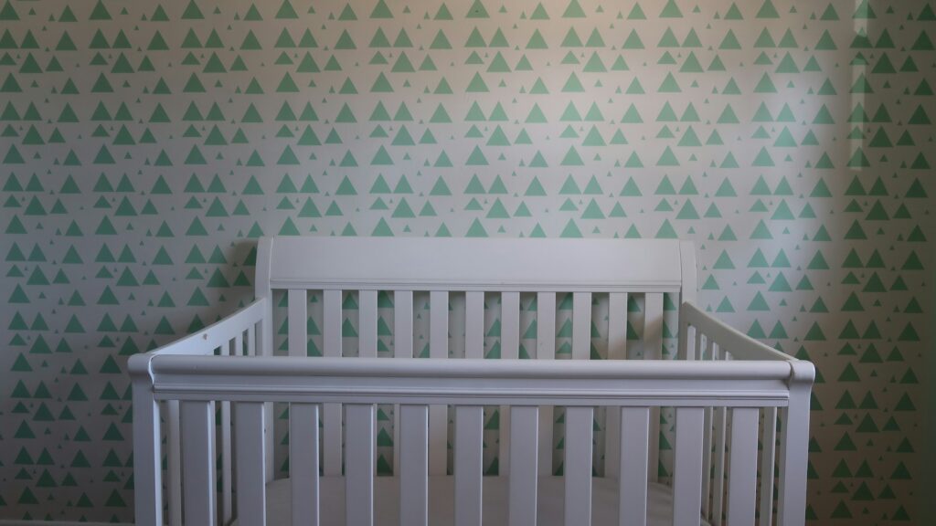 A white wooden crib in a nursery with a patterned wall.