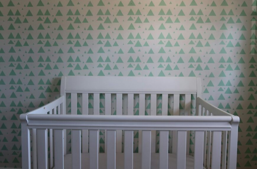 A white wooden crib in a nursery with a patterned wall.