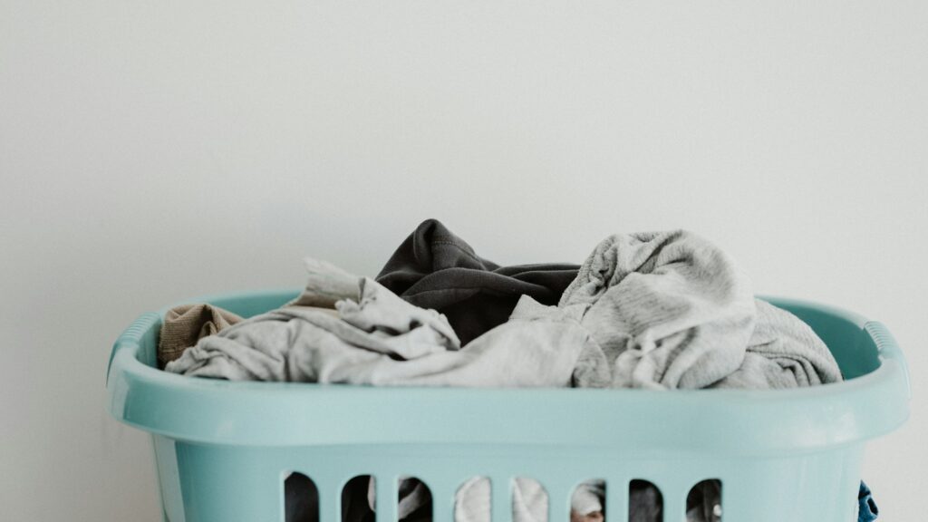 A blue laundry basket holds a pile of clean white clothes.