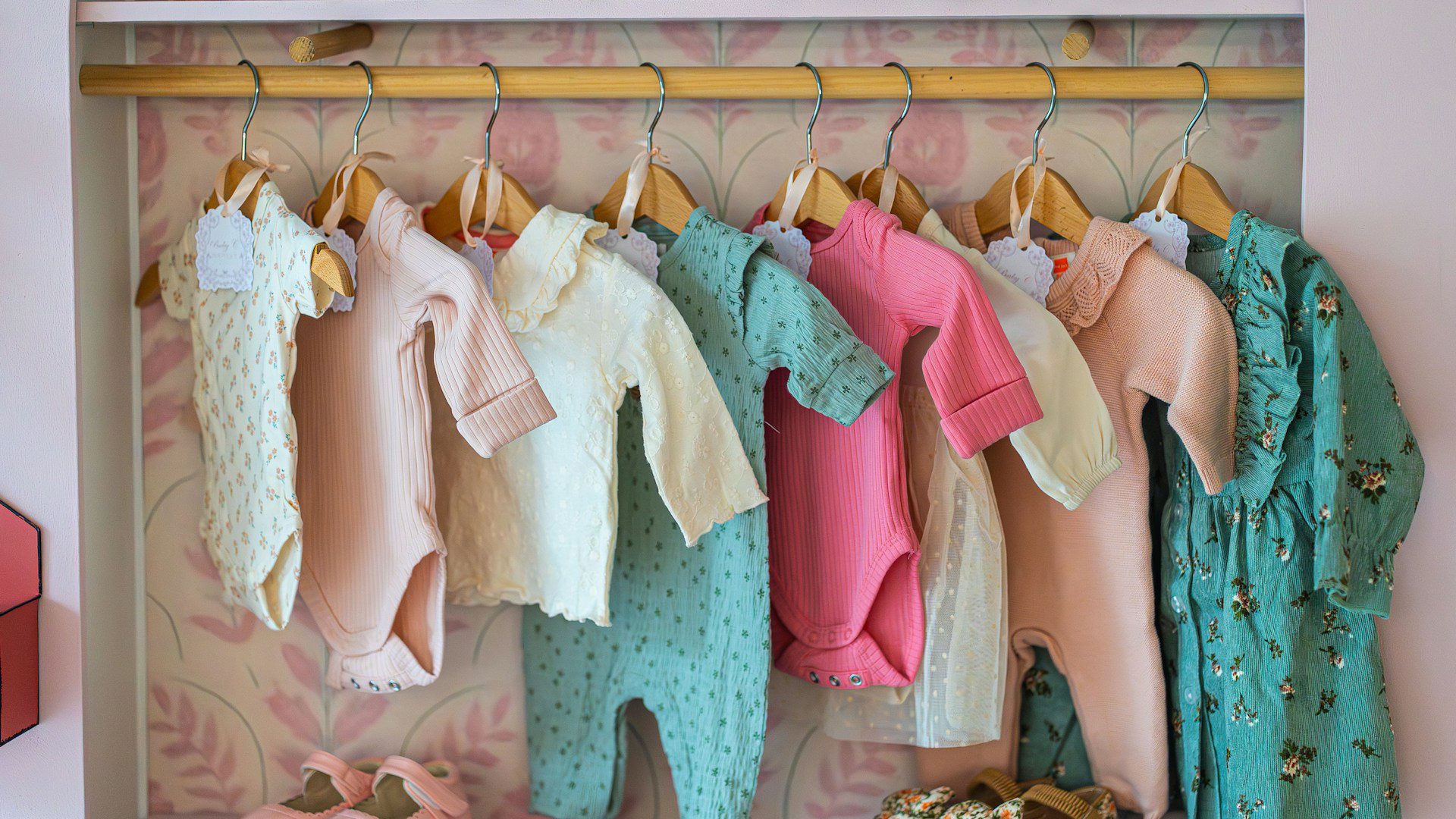Small children's clothes hang on a rack above a row of shoes.