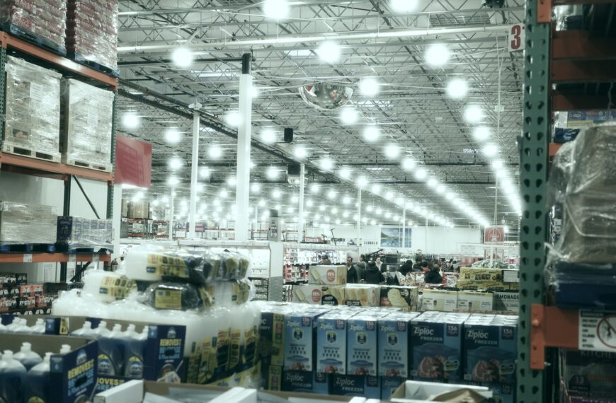 A wide aisle stretches through a brightly lit warehouse store.