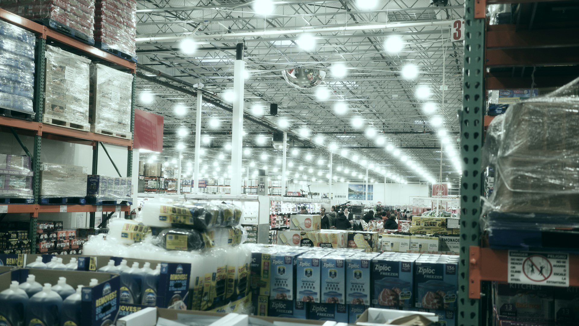 A wide aisle stretches through a brightly lit warehouse store.