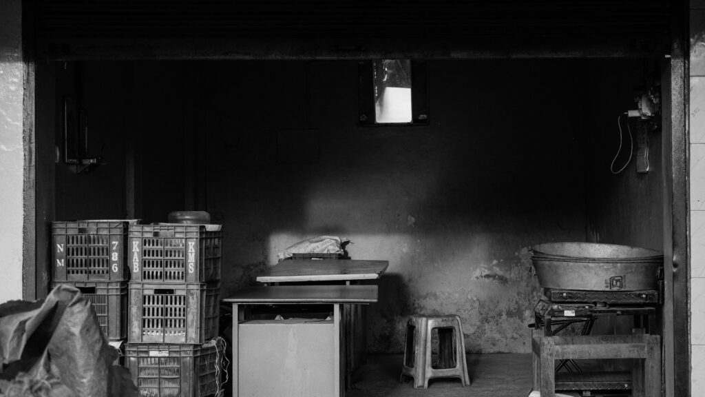 A stack of plastic storage crates sits beside tables in a dim room.