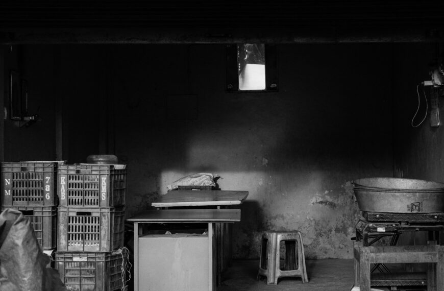 A stack of plastic storage crates sits beside tables in a dim room.