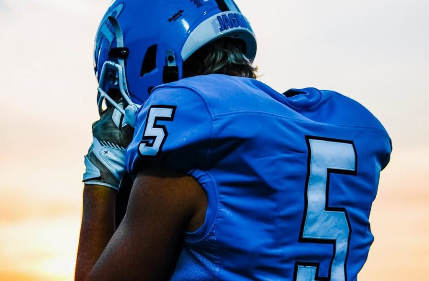 A football player in a blue number 5 jersey and helmet, seen from behind at sunset.